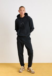 Sort hættetrøje og matchende sweatpants lavet af blødt bomuldsblanding, med en lommesæk foran og snore, parret med multicolor sneakers.