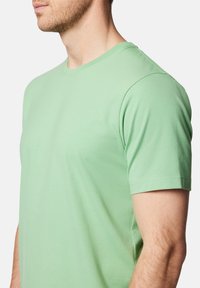 Jasnozielony t-shirt z okrągłym dekoltem wykonany z miękkiego, gładkiego materiału, z krótkimi rękawami i luźnym krojem. Prosty design bez wzorów czy dodatków.