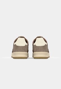 Brown suede sneakers with white detailing, featuring a padded collar and textured rubber sole. Branding is embossed on the heel.