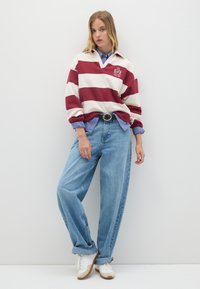 Maglietta a righe in stile rugby bianca e bordeaux, sovrapposta a una camicia a quadri blu. Jeans larghi di un leggero blu e sneakers bianche completano il look.