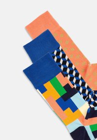 Mehrfarbige Socken im Set: eine orangefarbene mit goldenen Punkten, eine blaue und eine gemusterte mit geometrischen Formen in blau, grün, gelb und schwarz.