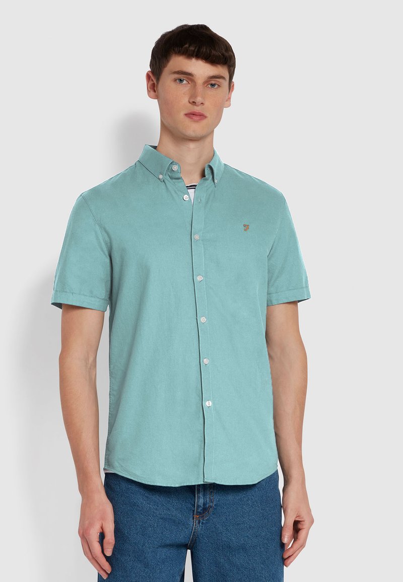 Korte mouwen, knoopsluiting overhemd van licht teal stof, met een kraag, witte knopen en een klein geborduurd logo op de borst.