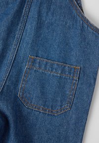 Denimstof in donkerblauw met een rechthoekige achterzak. Kenmerkt zich door geel-oranje stiksel en een gladde textuur. Eenvoudig, strak ontwerp.