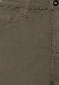Calças de denim verde-oliva com uma textura suave, detalhes de costura, bolsos padrão e um fecho de botão metálico na cintura.