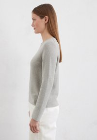 Grijze geribbelde trui met een ronde hals en lange mouwen, gecombineerd met witte broek. Soepele textuur, aansluitend ontwerp en neutrale kleur.