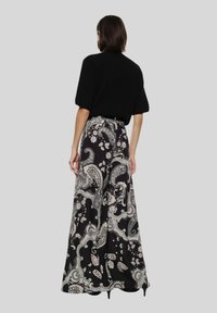 Top nero a maniche corte abbinato a una gonna lunga e fluida con una stampa paisley nera e crema. La gonna ha un punto vita con cintura.