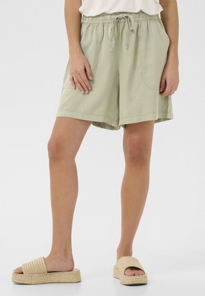 Shorts en coton vert clair avec une taille élastique et un cordon de serrage, dotés de deux poches latérales et d'une coupe ample, arrivant au-dessus du genou.