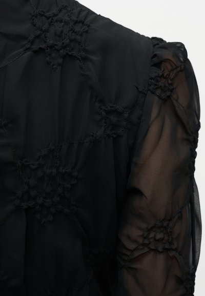 Bluza neagră cu țesătură transparentă, detalii florale brodate, accente texturate și mâneci adunate, creând un aspect stratificat.