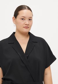 Μαύρο πουκάμισο με κοντά μανίκια, φτιαγμένο από υλικό με υφή. Διαθέτει κολάρο με εγκοπή και κομψό σχέδιο με ελαφριά λαμπερή υφή.