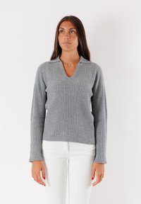 Maglione grigio a coste con scollatura a V e maniche leggermente a campana. Indossato con pantaloni bianchi, che mostrano un tessuto a maglia strutturato e una vestibilità rilassata.