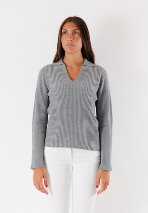 Maglione grigio a coste con scollatura a V e maniche leggermente a campana. Indossato con pantaloni bianchi, che mostrano un tessuto a maglia strutturato e una vestibilità rilassata.