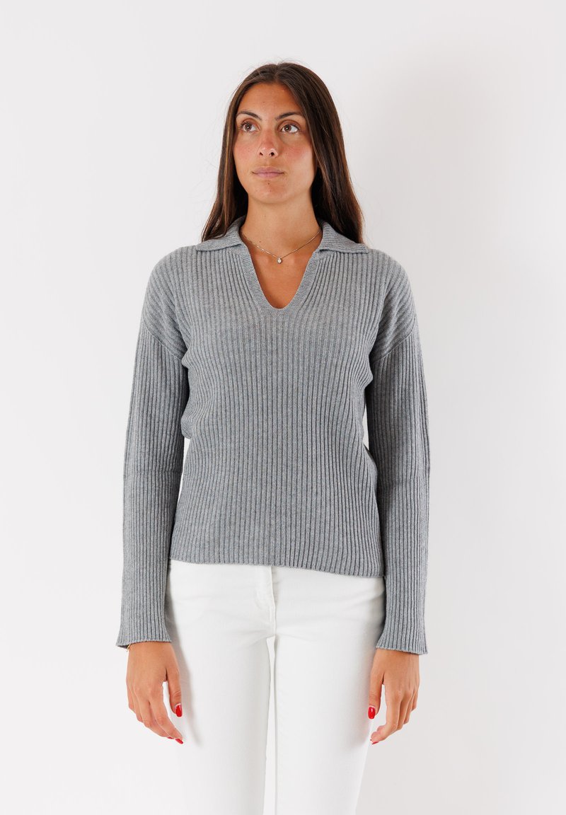 Maglione grigio a coste con scollatura a V e maniche leggermente a campana. Indossato con pantaloni bianchi, che mostrano un tessuto a maglia strutturato e una vestibilità rilassata.