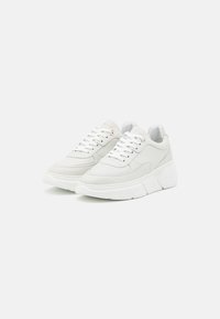 Sneakers bianchi con tomaia in pelle liscia, punta rotonda, suola spessa bianca e cuciture decorative. Occhielli metallici e logo accentato sulla linguetta.