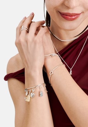 Silberschmuck mit mehreren Charms-Armbändern, zarten Ringen und einem Choker. Auffällige Charms sind ein Herz, ein Schlüssel und ein Gummibärchen.