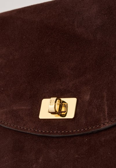 Gros plan sur un rabat de sac en daim marron avec une fermeture métallique dorée rectangulaire à verrouillage tournant.