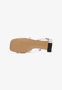 Sandale plate blanche avec un bout carré, de fines lanières et un talon bas texturé noir. Semelle lisse avec une finition beige. Design minimaliste.