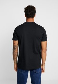 Zwarte katoenen t-shirt met korte mouwen, een ronde hals en een zachte textuur, gedragen met blauwe jeans, met zichtbare armtattoos.