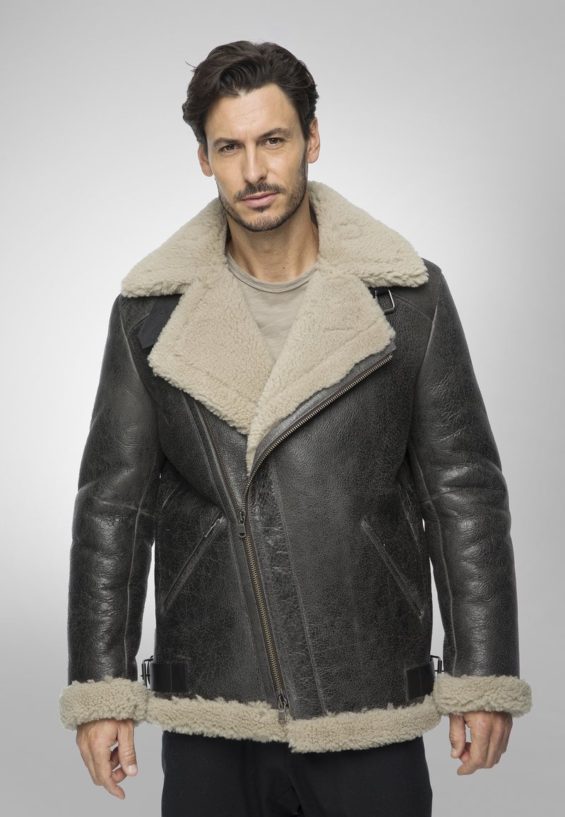 Giubbotto di pelle nera con colletto e polsini in shearling beige, con zip diagonale e tasche laterali. Finitura testurizzata con accenti lisci.