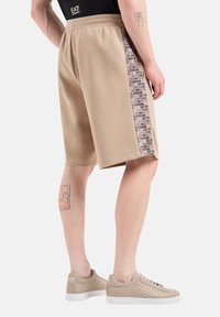 Beige sportos rövidnadrág, texturált felülettel, logóval ellátott oldalsó panellel, rugalmas derekúval és laza szabással.
