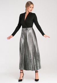 Czarna bluzka z długim rękawem w białe kropki, zestawiona z plisowaną srebrną metaliczną spódnicą, uzupełniona czarnymi szpilkami.