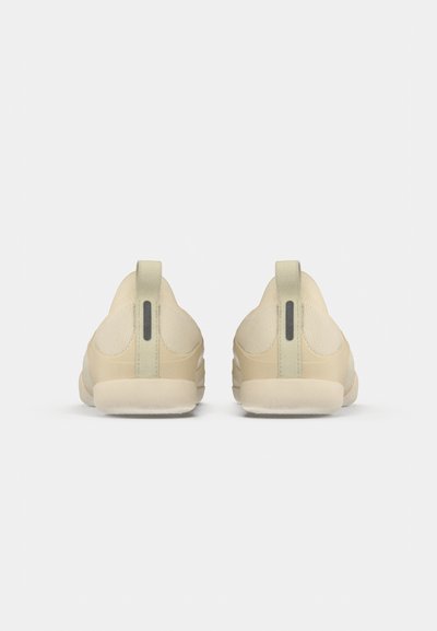 Een paar beige instappers gezien van achteren, met stoffen trek-lussen en zwarte verticale reflecterende strepen.