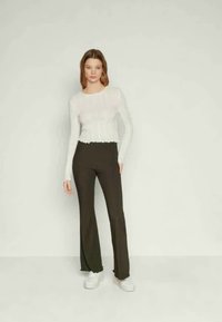 Top branco com mangas longas e bainha ondulada, combinado com calças pretas largas de cintura alta. Modelo usa ténis brancos.