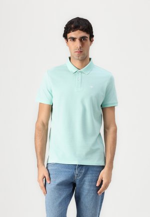 Polo léger vert avec un col, deux boutons, des manches courtes et un petit logo. Porté avec un jean en denim bleu.