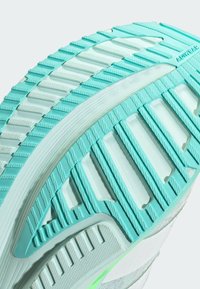 Lichte atletische schoenzool in teal en wit, met gestructureerde grippatronen, een gebogen ontwerp en ventilatie-openingen voor ademend vermogen.