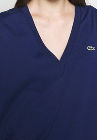 Navy blue V-neck t-shirt made of soft fabric, featuring a small embroidered crocodile logo on the left side. Simple design, short sleeves.