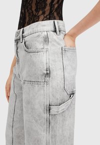 Pantalones de denim gris con un acabado ligeramente desgastado, que cuentan con bolsillos delanteros y un detalle de bolsillo trasero visible. Textura suave y corte holgado.