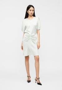 Φόρεμα ανοιχτό πράσινο σατέν με κοντά φουσκωτά μανίκια και μπροστινή λεπτομέρεια με στρίψιμο. Διαθέτει απαλό, μήκος μέχρι το γόνατο και μινιμαλιστικό σχέδιο.