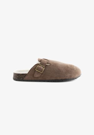 Pantofole in suede marrone con un interno imbottito e morbido, dotate di una fibbia metallica e suola in sughero testurizzata. Design a profilo basso.