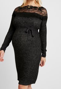 Abito nero in maglia con maniche lunghe, dettagli in pizzo sul colletto, vita aderente con cintura in tessuto e stoffa testurizzata.