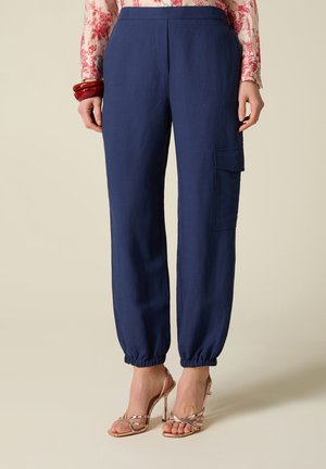 Kvinde iført marineblå cargobukser med elastiske ankler, røde armbånd, en blomstret langærmet top og rosa-guld højhælede sandaler.