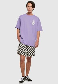 Purple cotton t-shirt with a white design, paired with black and white checkered shorts. Black sneakers complete the outfit.