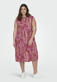 Abito midi fluido in rosa e crema con motivi floreali e a righe. Maniche corte e dettaglio al collo a chiave. Abbinato a sneakers bianche.