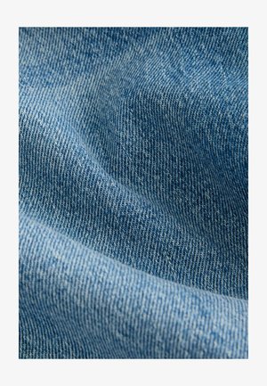 Denim tkanina u srednje plavoj boji, s teksturiranim tkanjem i vidljivim nitima. Površina prikazuje suptilne varijacije u boji i dubini.