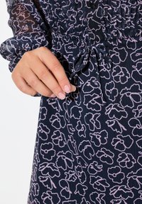 Marineblaues Kleid aus strukturiertem Stoff mit einem rosafarbenen Blumenmuster. Geraffte Taille mit einem Bindeband und langen Puffärmeln.