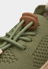 Πράσινο πλεκτό αθλητικό παπούτσι με πράσινα ελαστικά κορδόνια στερεωμένα με καφέ κουμπωτήρα στη γλώσσα.