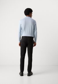 Chemise à manches longues bleu clair associée à un pantalon noir. La chemise a un col classique ; le pantalon présente un design épuré avec des poches arrière.
