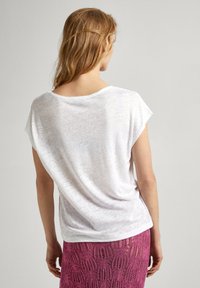 Camisa blanca, de corte holgado y mangas cortas, con un escote bajo en la espalda, hecha de un tejido ligero y texturizado, combinada con una falda de encaje rosa.