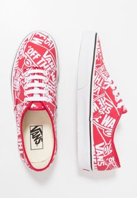 Rote Canvas Vans Sneakers mit einem ganzflächigen weißen Logo-Print, Schnürdesign, weißen Sohlen und schwarzen Akzentlinien entlang der Kanten.