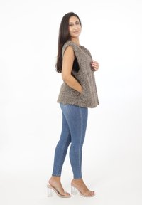 Faux fur ärmlös väst i taupe med en mjuk textur, med sidofickor. Pared med blå skinny jeans och genomskinliga klacksandaler.