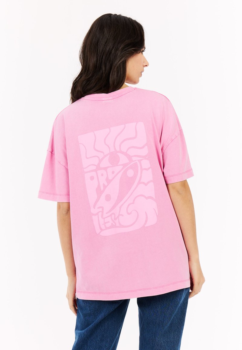 Roze oversized t-shirt met een grote witte grafische print op de rug, met abstracte lijnen, een raket en golven.