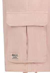 Lichtroze jacketstof met gestikte naden, voorzien van een voorzak met een flap en een label met de tekst "SBLVL Sublevel voor modefans."