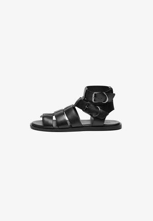 Sandal em couro preto com várias tiras, detalhes em fivela, design de ponta aberta, sola plana e textura suave.