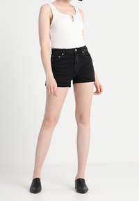 Musta denimshortsit korkealla vyötäröllä ja viiden taskun mallilla, yhdistettynä valkoiseen ribbineuletankkitoppiin, jossa on pyöreä pääntie. Asun täydentävät mustat mules-kengät.