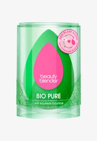 Spugna da trucco verde a forma di uovo, confezionata in un contenitore trasparente e cilindrico. Presenta un logo e un'etichetta rosa che indicano il 60% di materiale vegetale.