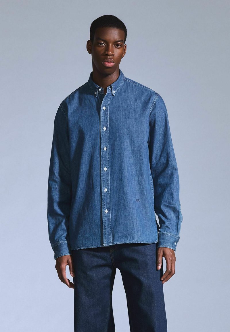 Camicia in denim blu scuro con colletto, maniche lunghe e bottoni bianchi. Abbinata a pantaloni in denim blu scuro.