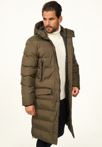 Langer, olivgrüner Steppmantel mit Kapuze, Reißverschluss vorne und zwei Vordertaschen; mit gestepptem Muster und schwarz gefüttertem Innenfutter.